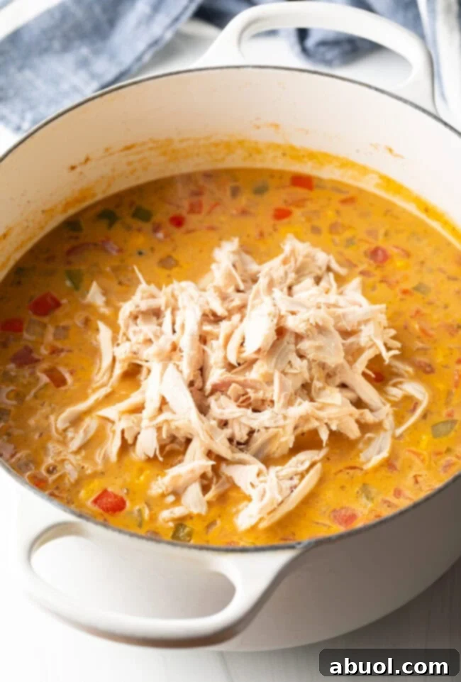 Creamy chicken, bean, and corn soup gently simmering in a white pot on the stovetop.