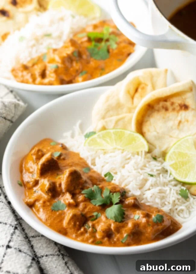 Creamy Lamb Tikka Masala 2 Deep white plate half filled with lamb tikka masala, and half with white rice. Two pieces of naan and two slices of lemon are on the side of the plate.