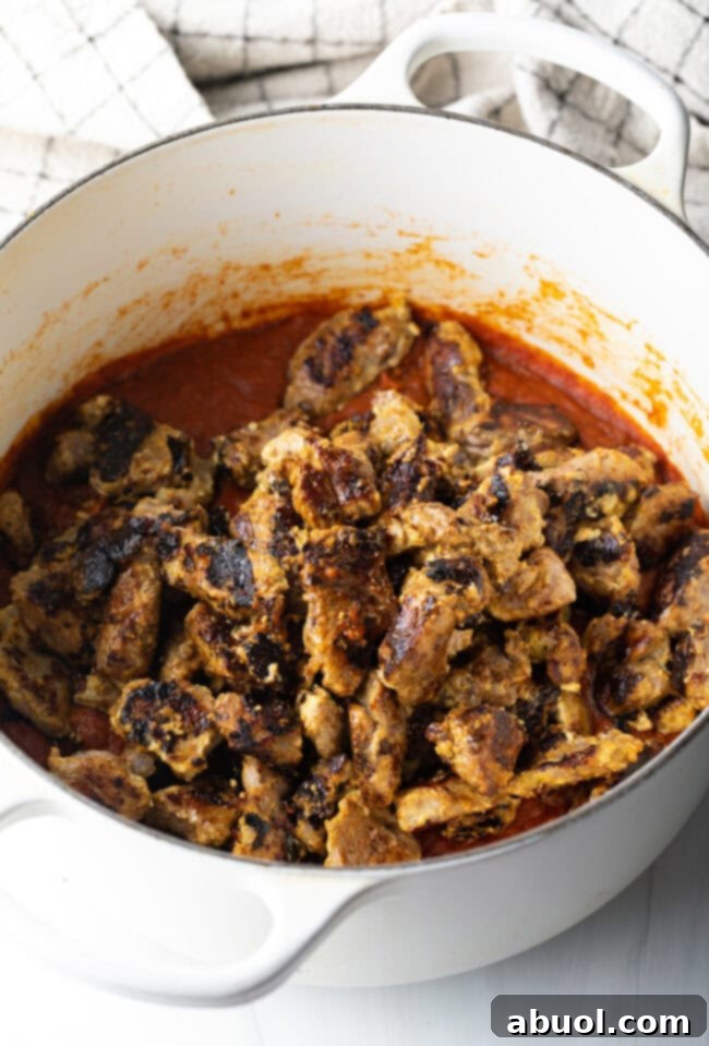 Creamy Lamb Tikka Masala 11 Seared pieces of lamb meat in a white cooking pot with tomato sauce.