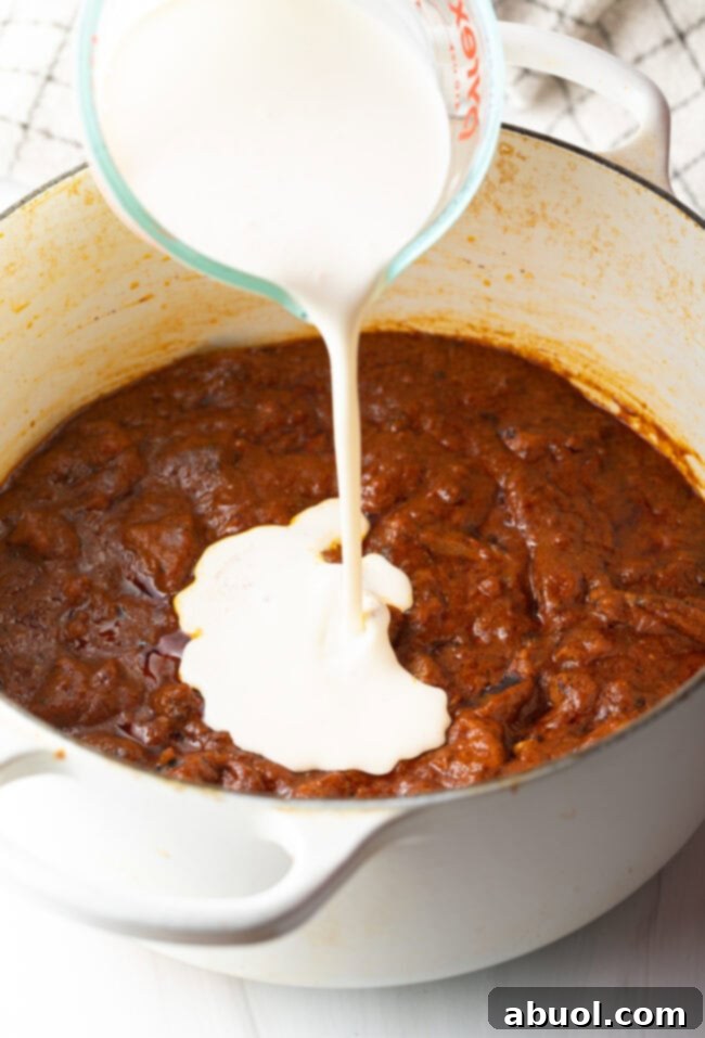 Creamy Lamb Tikka Masala 12 Pouring cream from a glass measuring cup into the lamb and tomato sauce.