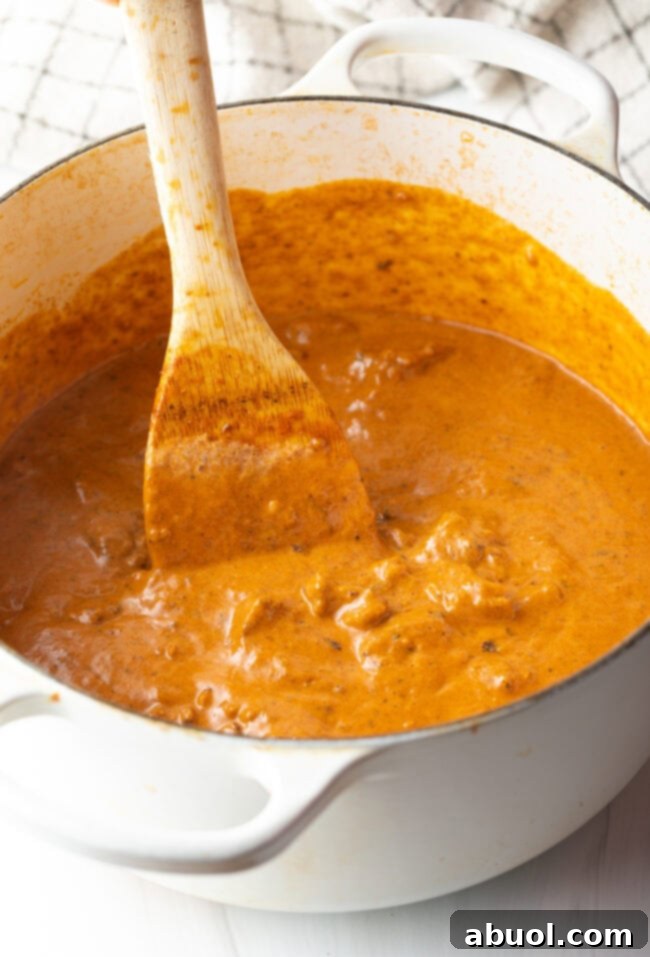 Creamy Lamb Tikka Masala 13 Wooden spoon stirring lamb curry sauce in a white pot.