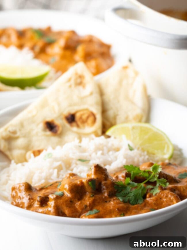Creamy Lamb Tikka Masala 14 Deep white plate half filled with lamb tikka masala, and half with white rice. Two pieces of naan and two slices of lemon are on the side of the plate.