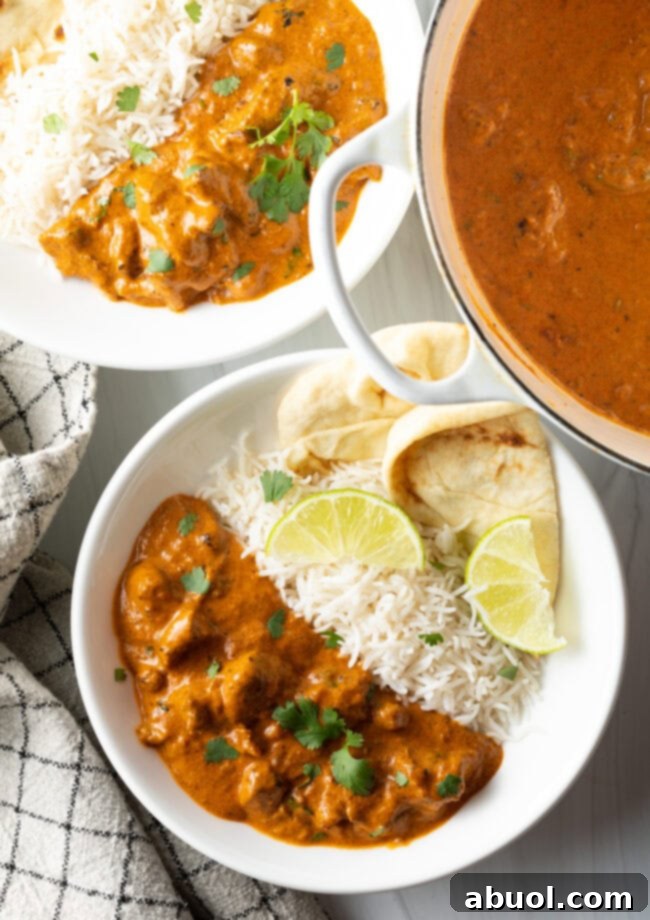 Creamy Lamb Tikka Masala 16 Deep white plate half filled with lamb tikka masala, and half with white rice. Two pieces of naan and two slices of lemon are on the side of the plate.