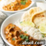 Deep white plate half filled with lamb tikka masala, and half with white rice. Two pieces of naan and two slices of lemon are on the side of the plate.