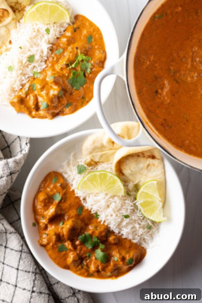 Creamy Lamb Tikka Masala 4 Deep white plate half filled with lamb tikka masala, and half with white rice. Two pieces of naan and two slices of lemon are on the side of the plate.