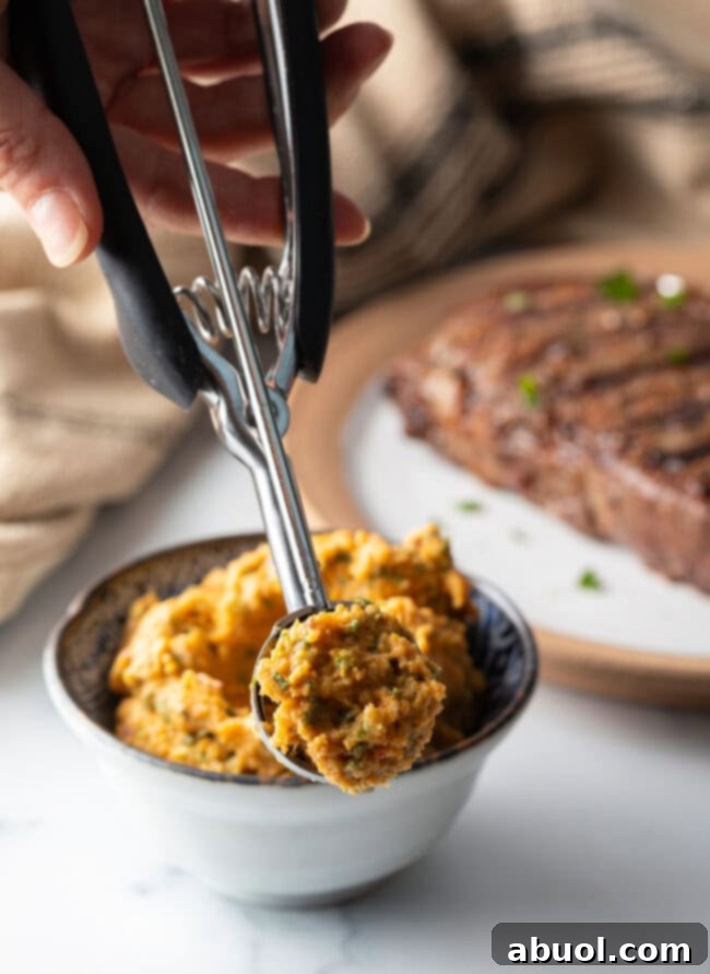 Hand with small metal cookie dough scoop, showing scoop of cowboy compound butter to camera.