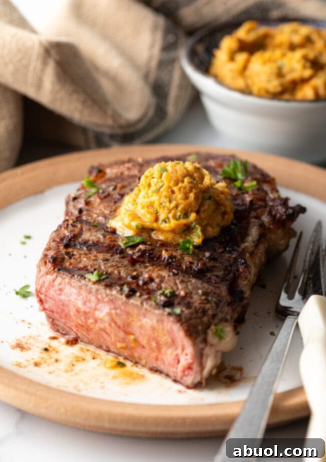 Perfectly grilled steak cut in half to show medium rare inside. The steak is topped by a scoop of compound butter.