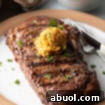 Grilled steak on a white plate with scoop of spiced compound cowboy butter on top.