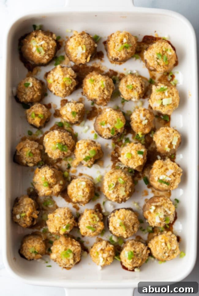 Top down view, two dozen seafood stuffed mushrooms with ritz crackers in a white baking dish.