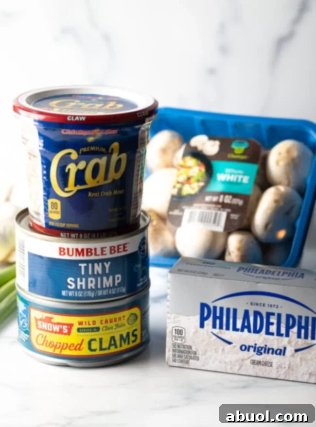 Recipe ingredients: Can of clams, tiny shrimp, and tub of crab stacked on top of each other. A package of cream cheese and package of white mushrooms are next to the stack.