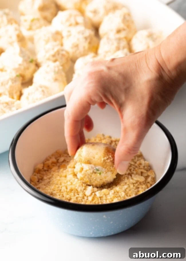 Hand rolling a stuffed mushroom in a bowl of crushed Ritz crackers.