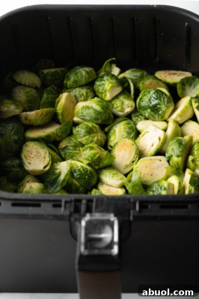 Uncooked sprout halves in an air fryer basket.
