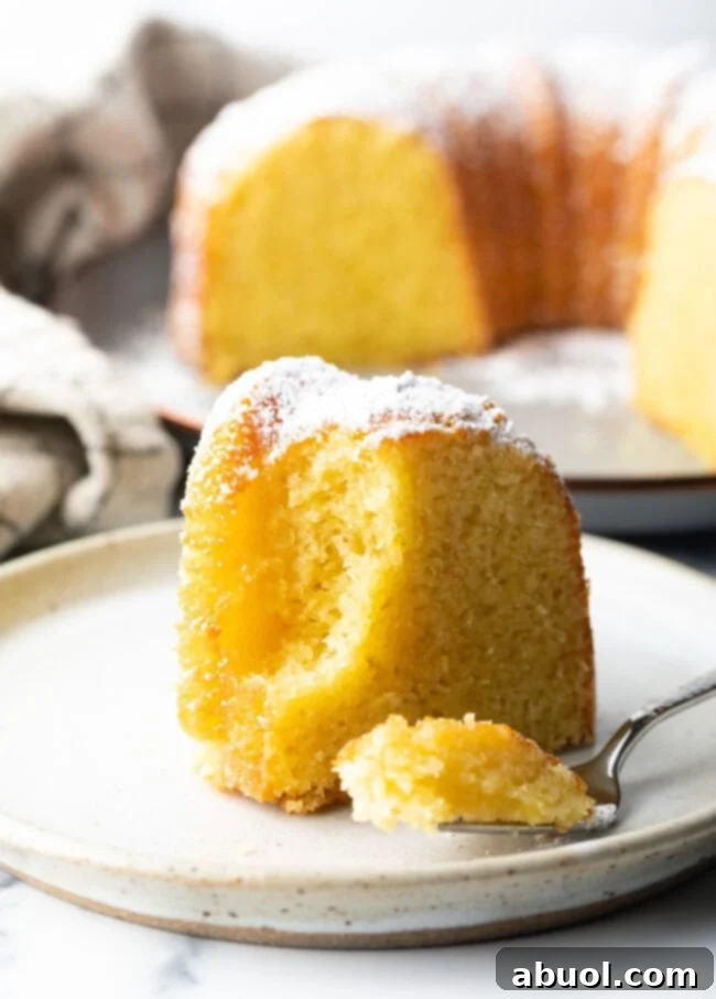 Golden Lemon Olive Oil Cake 11 A delectable slice of yellow cake on a white plate, with a fork poised to take a bite, highlighting its inviting texture.