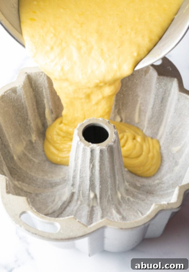 Golden Lemon Olive Oil Cake 7 Thick, golden lemon olive oil cake batter being carefully poured into a meticulously prepared Bundt pan.