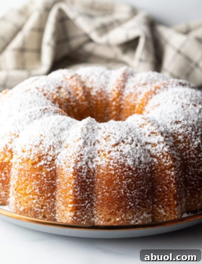 Golden Lemon Olive Oil Cake 9 A beautifully decorated lemon olive oil bundt cake, generously dusted with powdered sugar, sitting on a white plate.