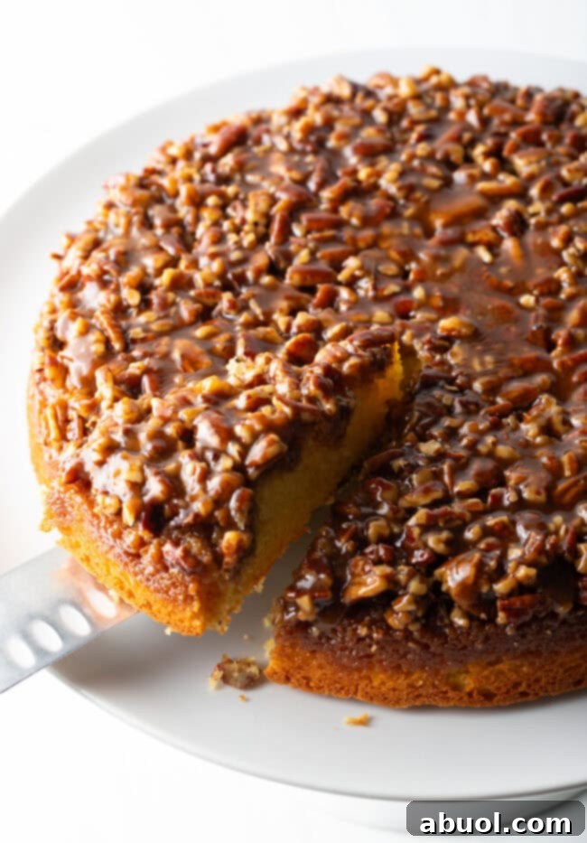A serving knife gently lifts a perfect slice of Pecan Upside Down Cake from the whole cake, highlighting its moist crumb and rich topping.
