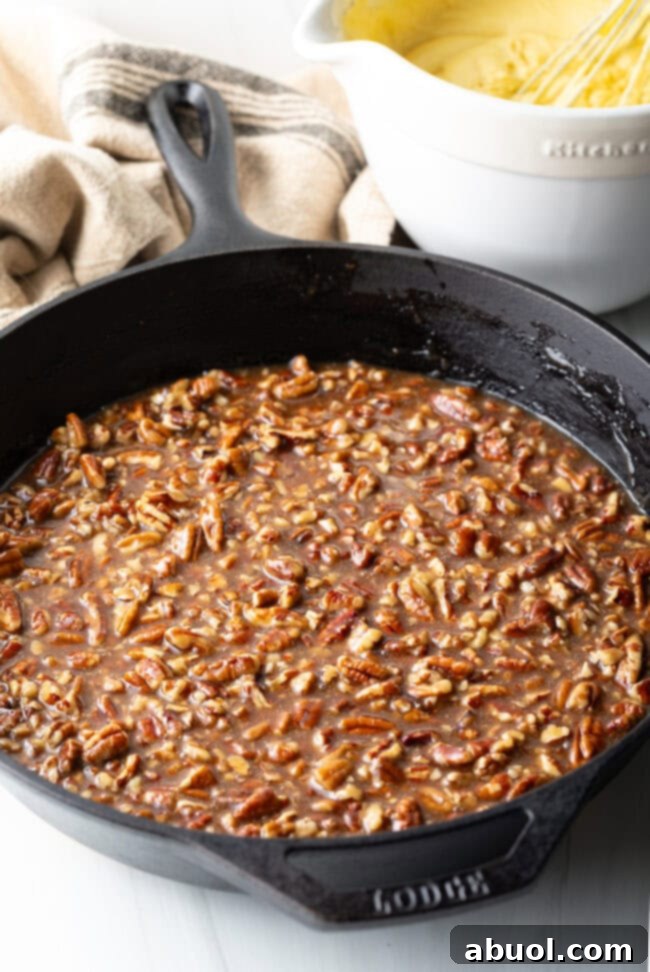 The pecan topping mixture, bubbling and caramelizing, in a cast iron skillet, showcasing its gooey texture.