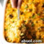 Broccoli cheese rice casserole in a white baking dish. A metal spoon is scooping a portion from the dish.