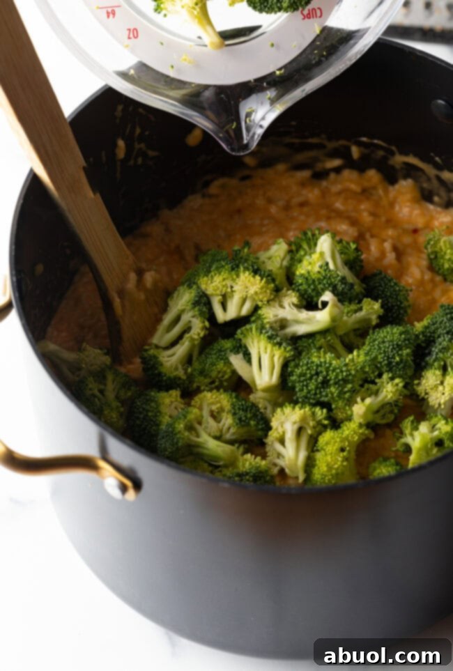 Broccoli florets and cheese in a pot with wooden spoon.