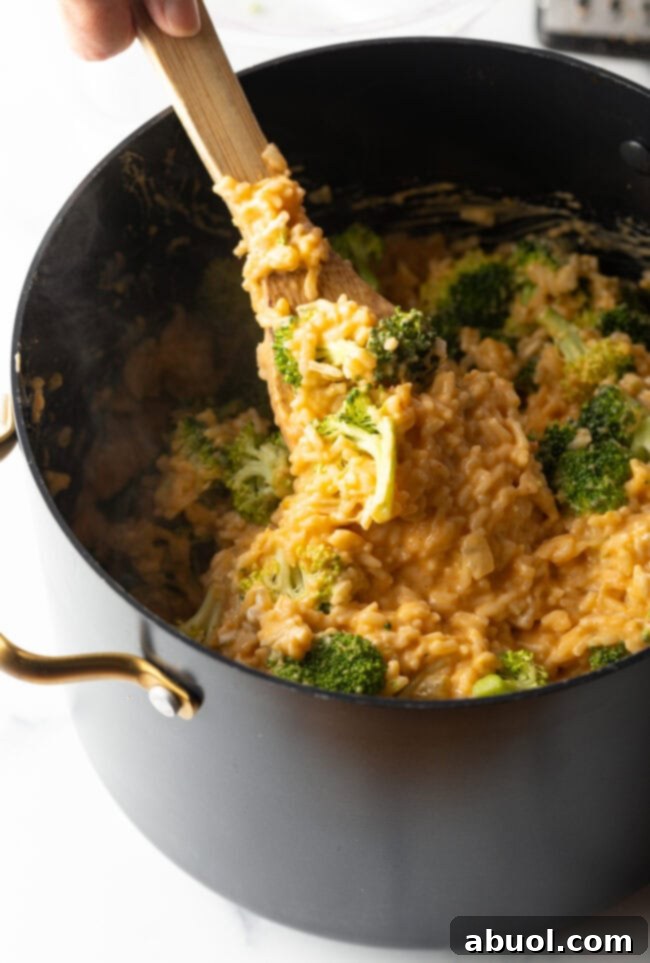 Spoon stirring mixture of rice, broccoli, and cheese in a pot.