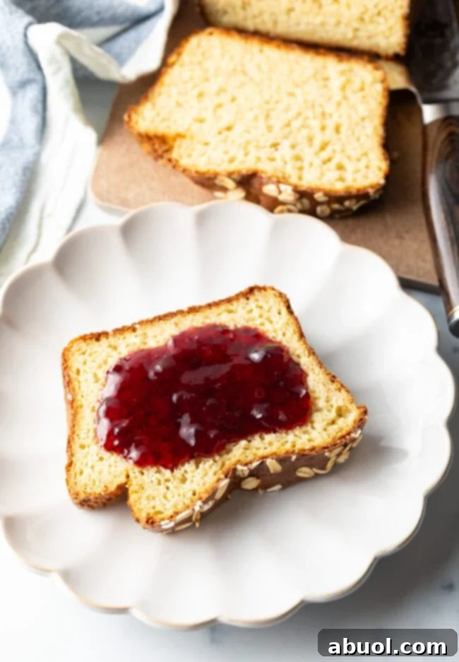 Slice of bread topped with red jelly, on a white plate.