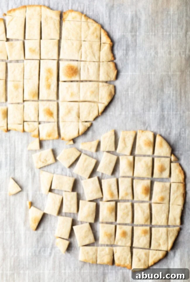 Two pieces of unleavened bread laying on a gray background. Each large oval of bread has been sliced into small squares.