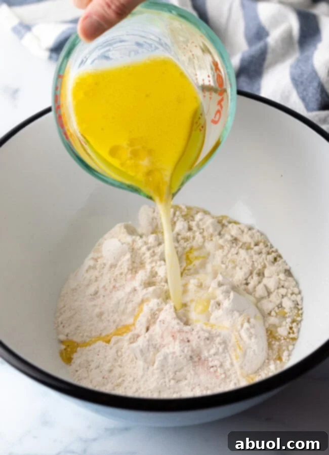 Adding melted butter to the flour mixture in a large white mixing bowl.
