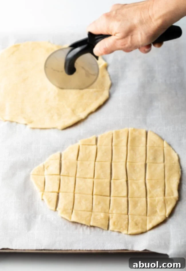 Hand with pizza cutter slicing two unbaked ovals of unleavened bread into tiny squares.