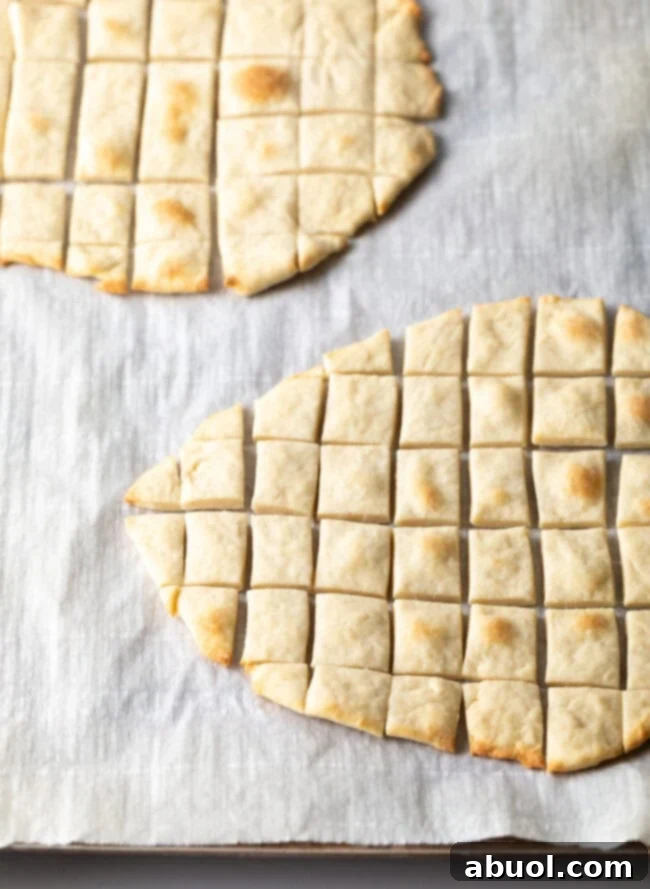 Two pieces of unleavened bread laying on a gray background. Each large oval of bread has been sliced into small squares.
