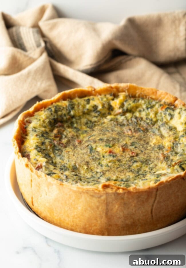 Baked veggie quiche with a deep dish crush on a white round plate.
