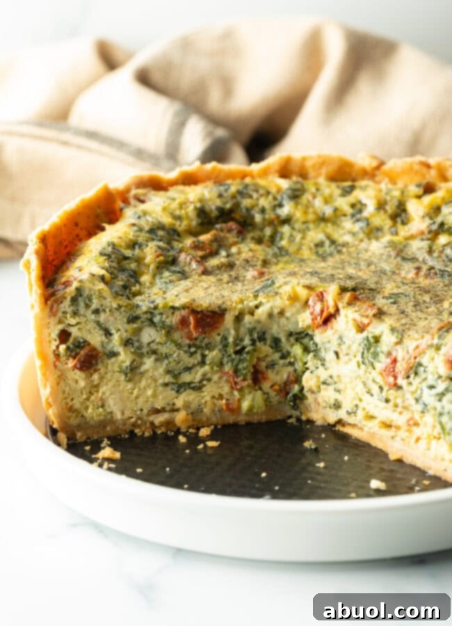 Baked veggie quiche with a deep dish crush on a white round plate. A large section has been cut out to show the vegetable-filled interior.