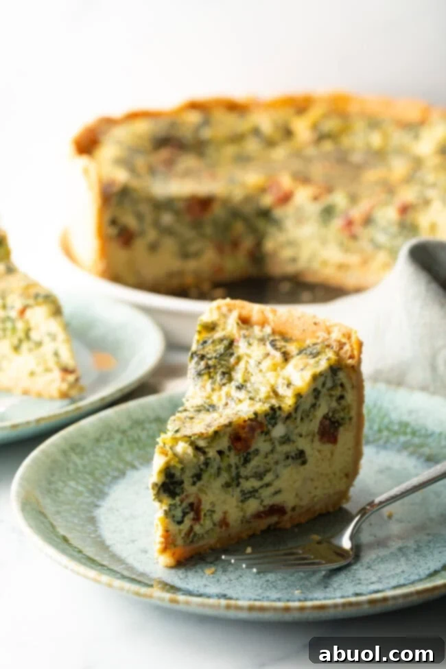Tall slice of quiche on a light blue plate. There is a fork to the side on the plate.