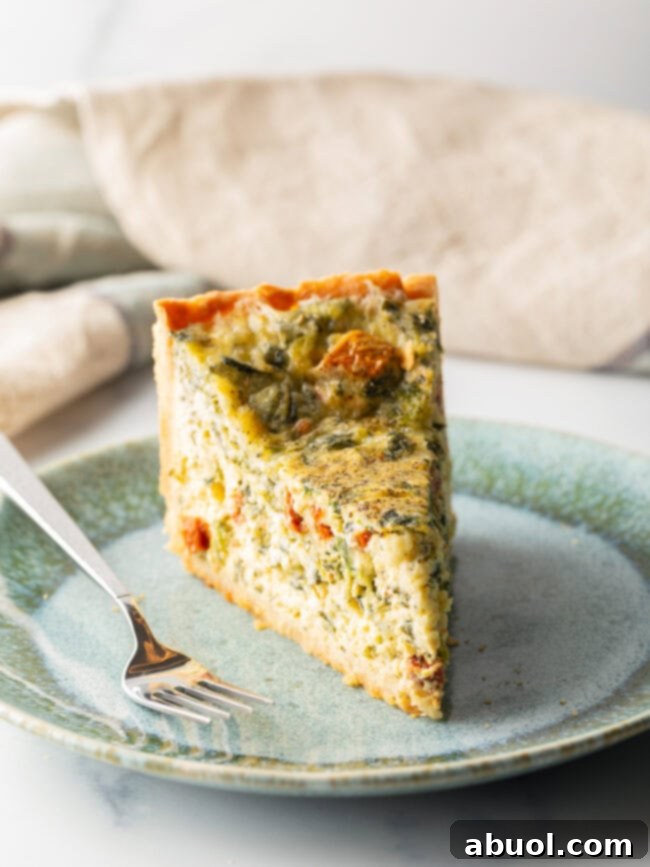 Tall slice of quiche on a light blue plate. There is a fork to the side on the plate.