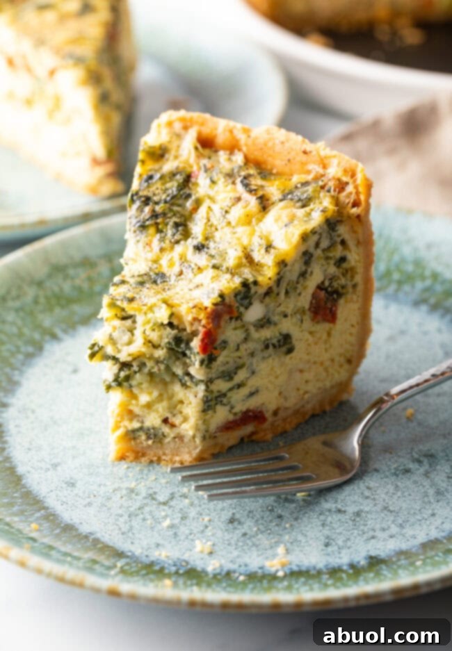 Tall slice of quiche on a light blue plate. A bite has been taken out of the tip of the slice, and there is a fork to the side on the plate.