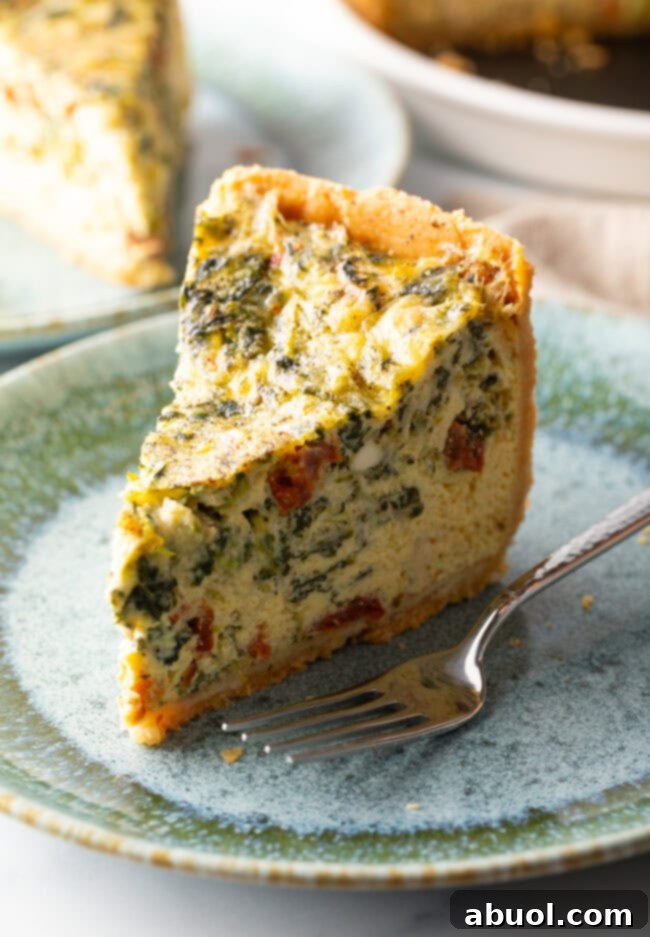 Tall slice of quiche on a light blue plate. There is a fork to the side on the plate.