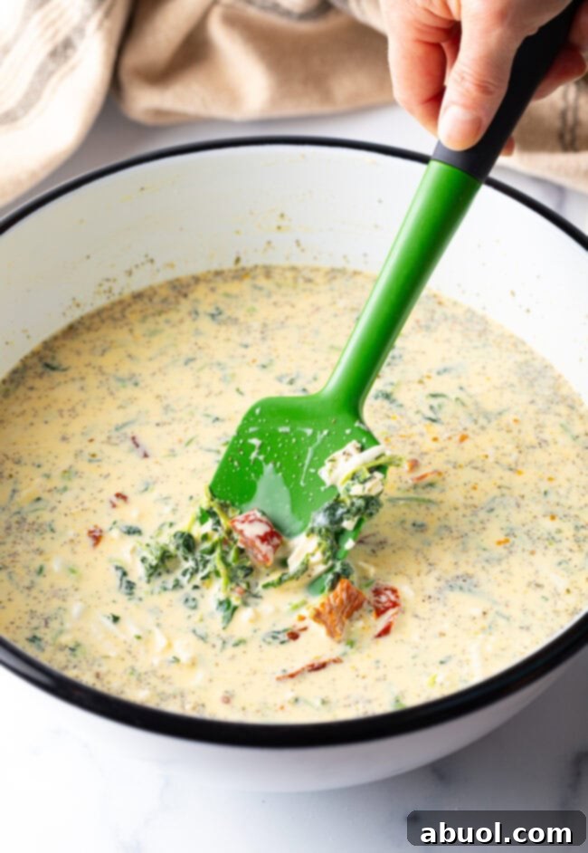 White mixing bowl with egg and veggie filling, being stirred with a green spatula.