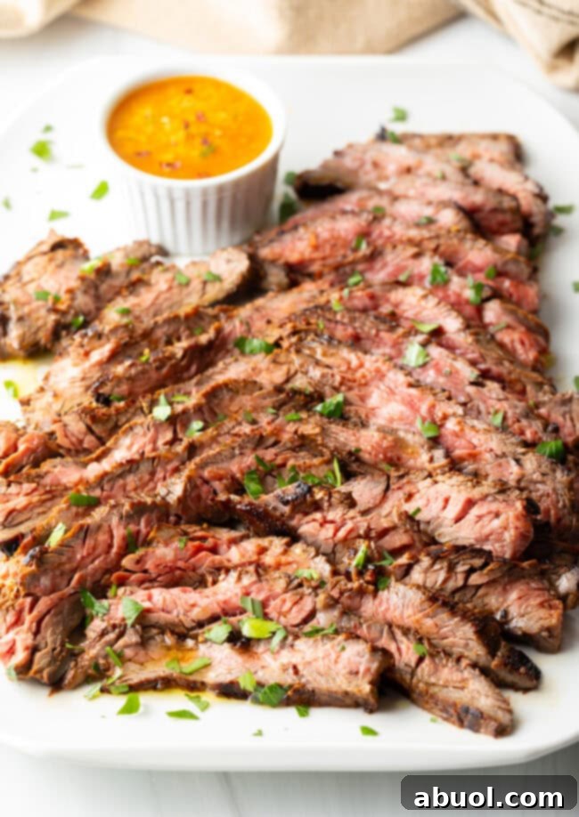 Thin slices of Bavette steak on a white serving platter with a ramekin of cowboy butter to the side.