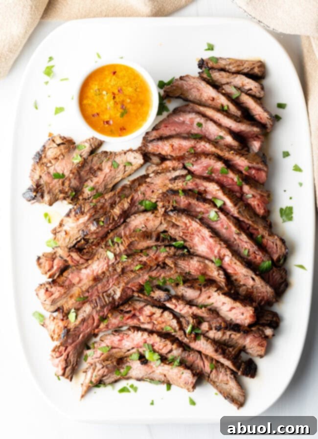 Thin slices of Bavette steak on a white serving platter with a ramekin of cowboy butter to the side.