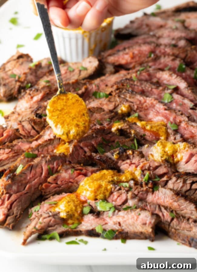 Hand spooning melted cowboy butter over thin slices of Bavette steak.