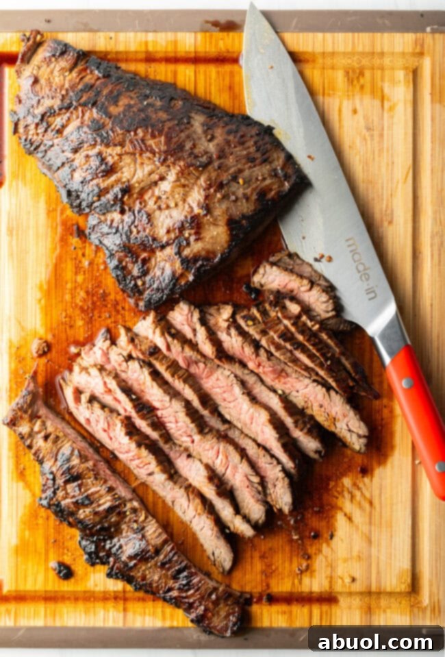 Seared steak sliced into thin strips on a wood cutting board, large knife to the side.