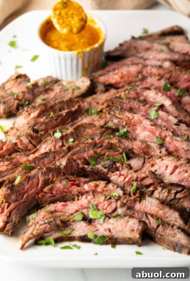 Thin slices of Bavette steak on a white serving platter with a ramekin of cowboy butter to the side.