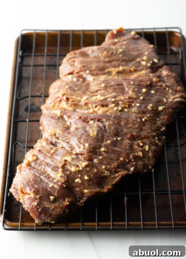 Raw large section of marinated beef on a wire rack.