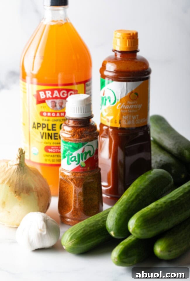 Recipe ingredients: Jars of apple cider vinegar, Tajin seasoning, and chamoy sauce. Also several small cucumbers, a whole onion, and head of garlic.