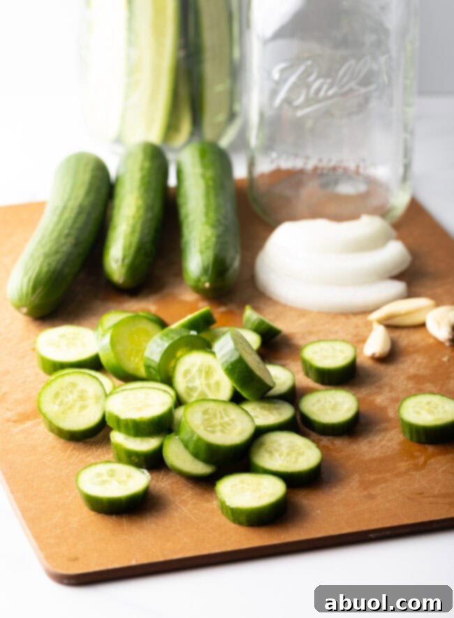 Wood cutting board with several small cucumbers, several sliced into thin rounds.