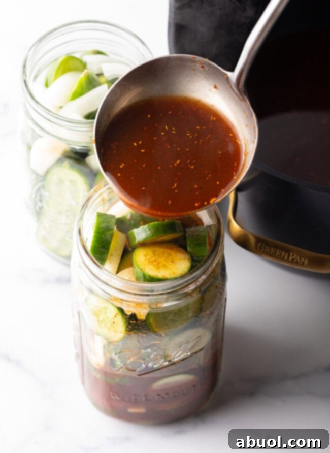 Pouring red liquid from a metal ladle into a glass jar filled with pickle slices.