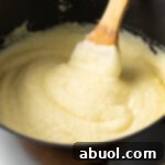 Creamy whipped potatoes in a black large pot, with a wooden spoon in the pot.