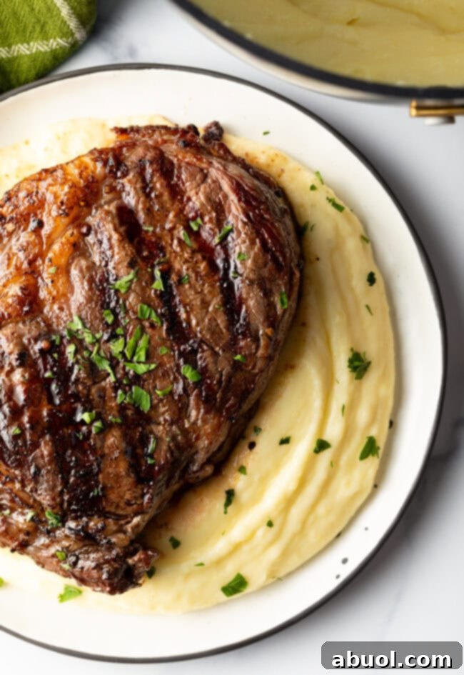 A succulent grilled steak is elegantly presented atop a velvety bed of whipped potatoes, ready to be savored.