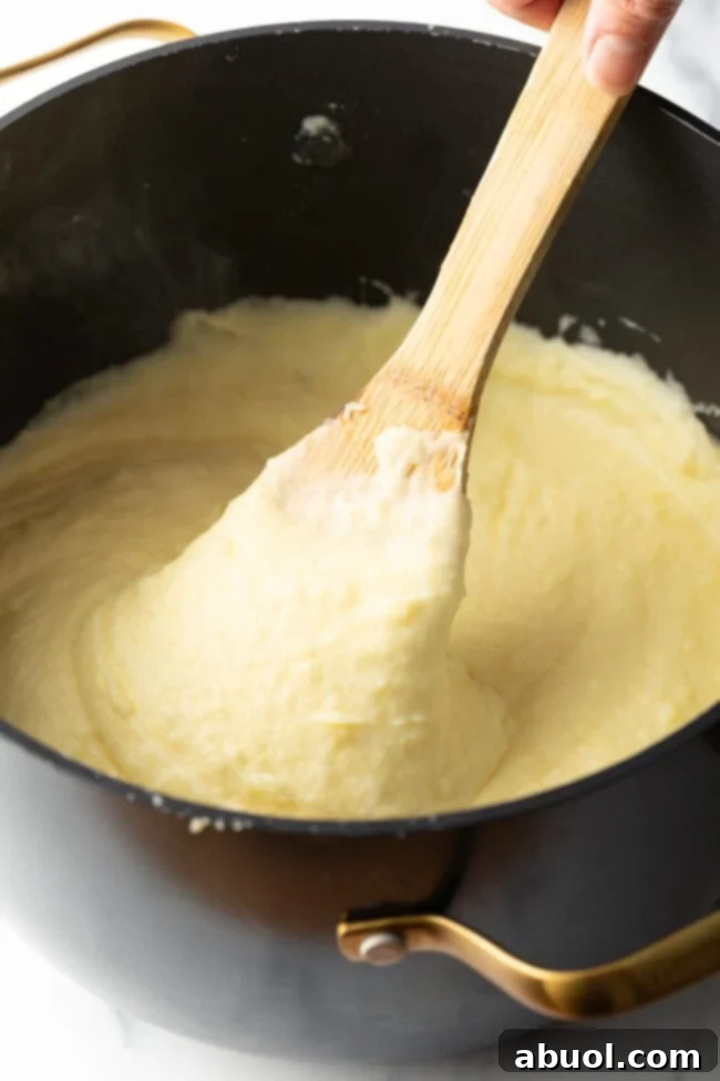 A wooden spoon rests in a large black pot, filled with perfectly creamy and whipped potatoes.