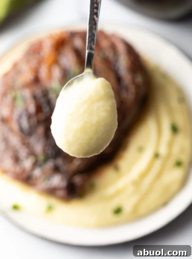 A close-up shot of a grilled steak on whipped potatoes, with a spoonful of the creamy potatoes lifted towards the camera, highlighting its smooth texture.