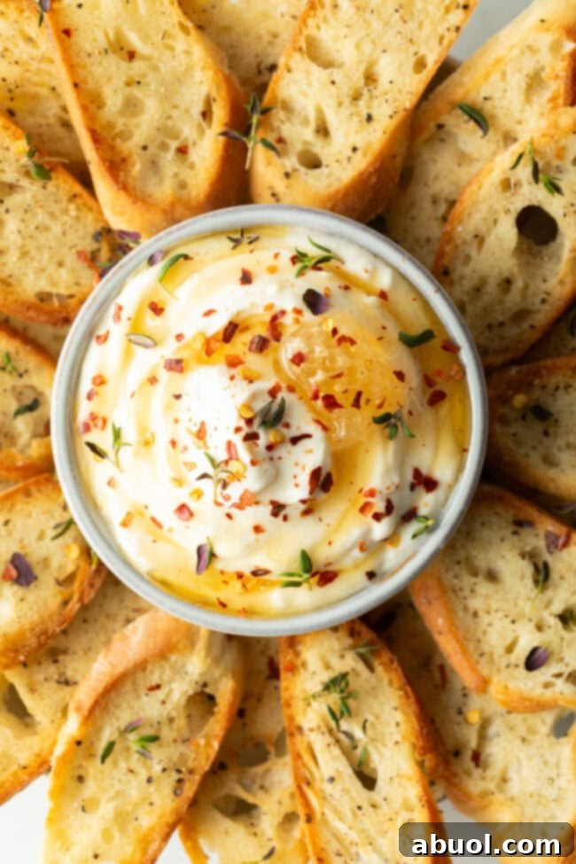 A beautiful bowl of fluffy whipped ricotta, garnished with honey and red pepper flakes, surrounded by toasted baguette slices arranged like flower petals, inviting a delicious dip.